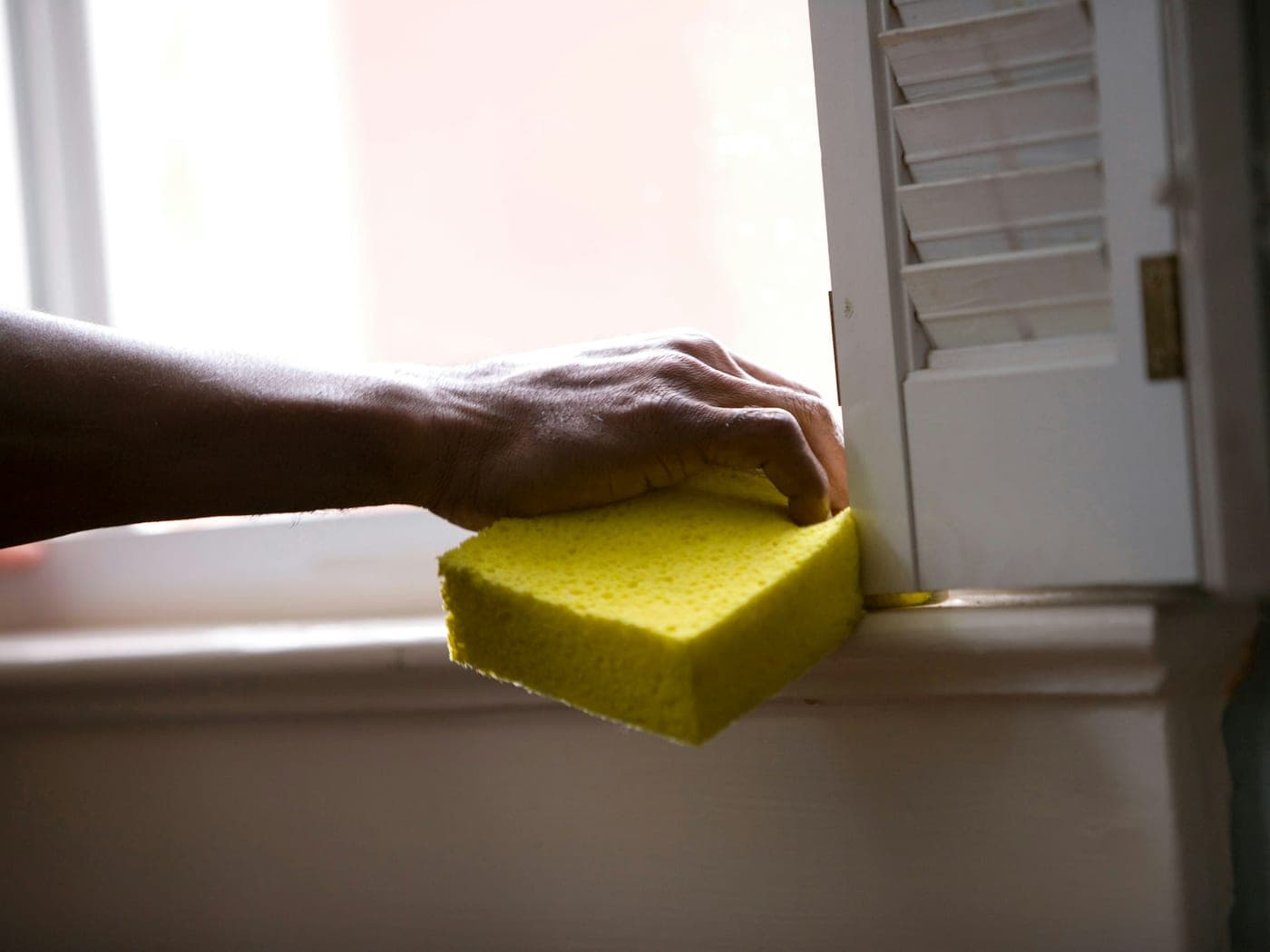 Main essuyant un encadrement de fenêtre à l'éponge jaune