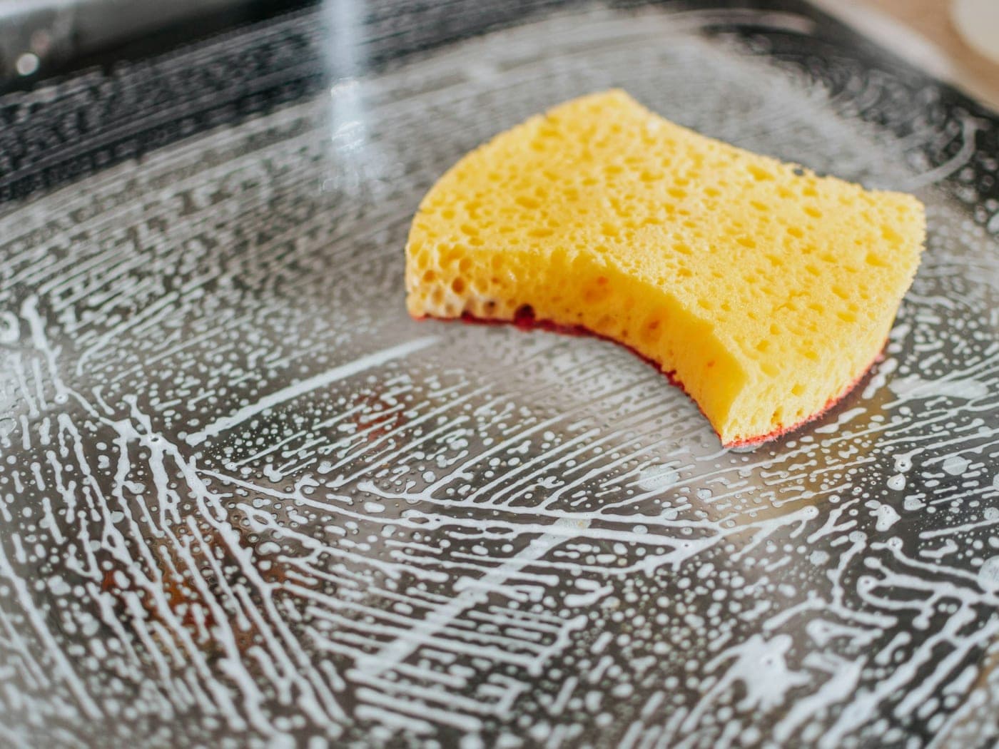 Éponge jaune frottant un plat couvert de mousse
