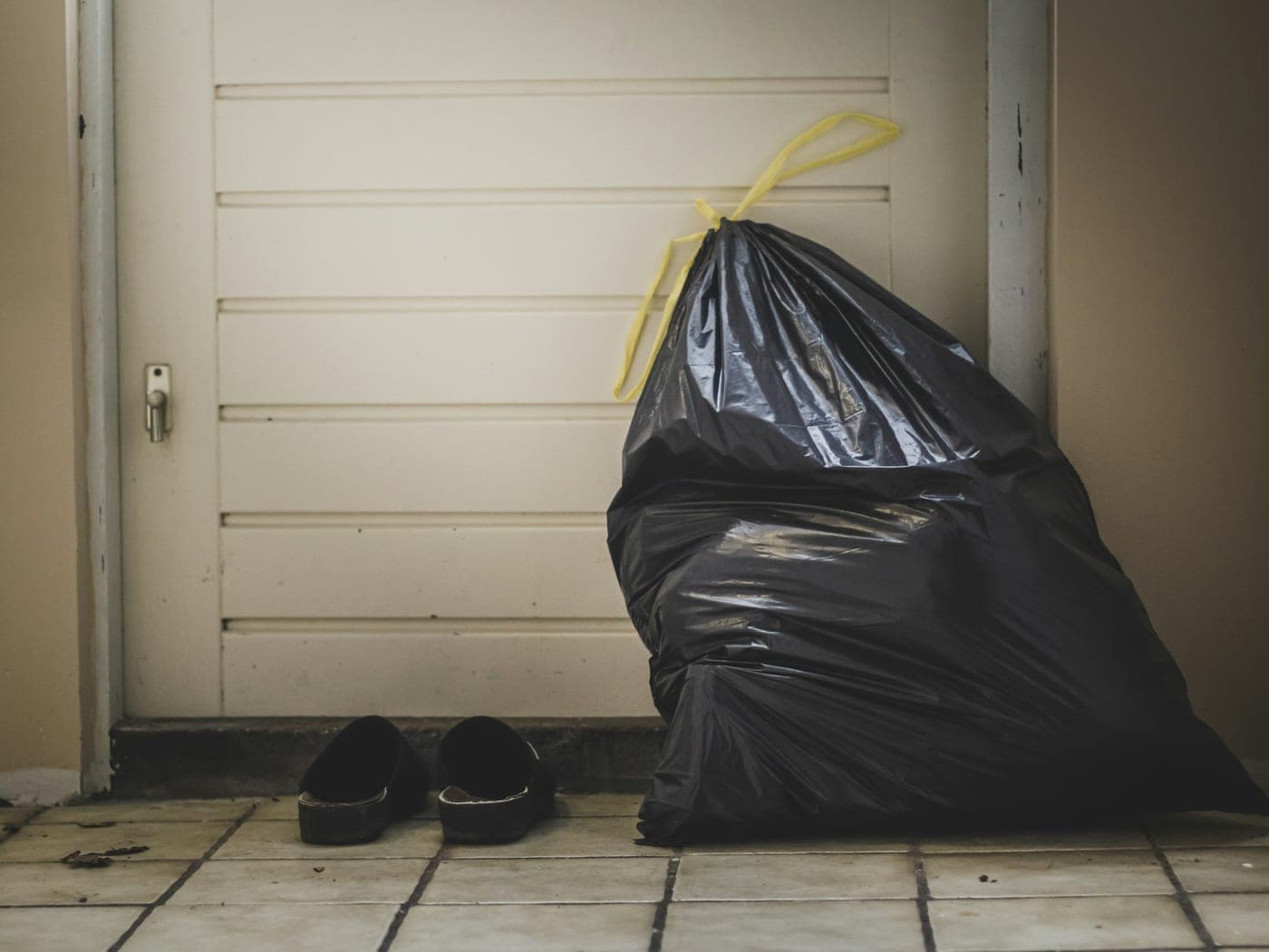 Sac poubelle fermé posé près d'une porte, sol carrelé