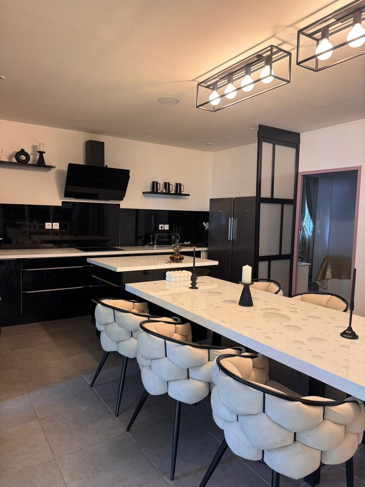 Cuisine ouverte noire et grande table blanche entourée de chaises