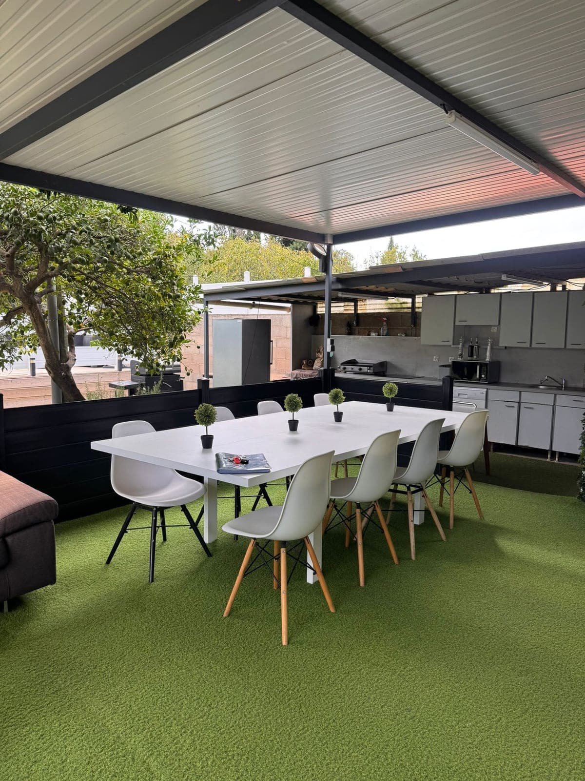 Terrasse couverte avec grande table blanche et chaises sur gazon synthétique