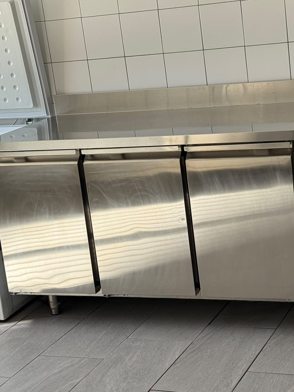 Meuble réfrigéré en inox à trois portes, propre, devant une faïence blanche